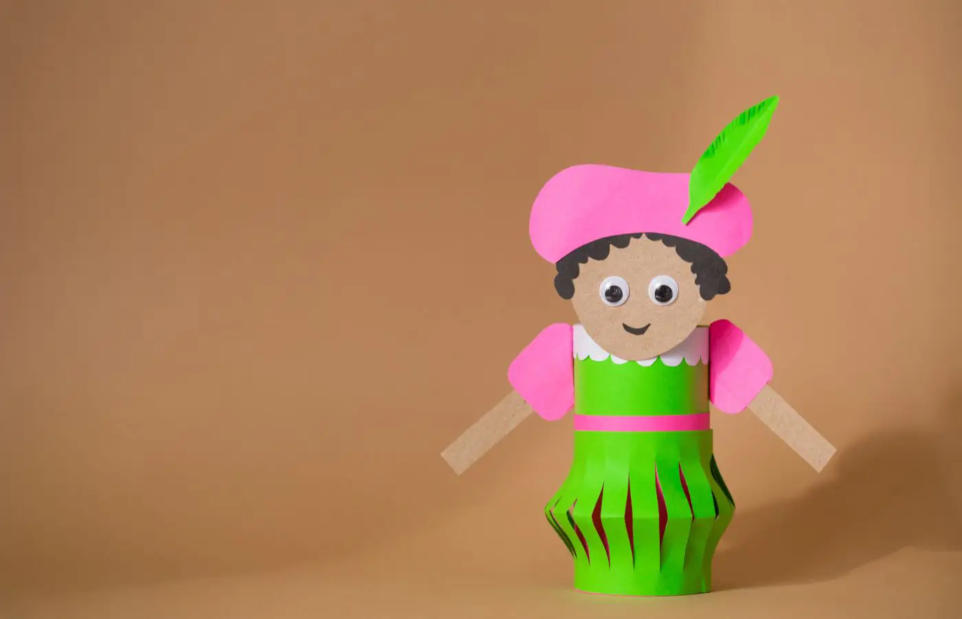 Handgemaakte Zwarte Piet knutselwerk, gemaakt van papier en karton, met een roze hoed, groene kleding en een vrolijke uitstraling.