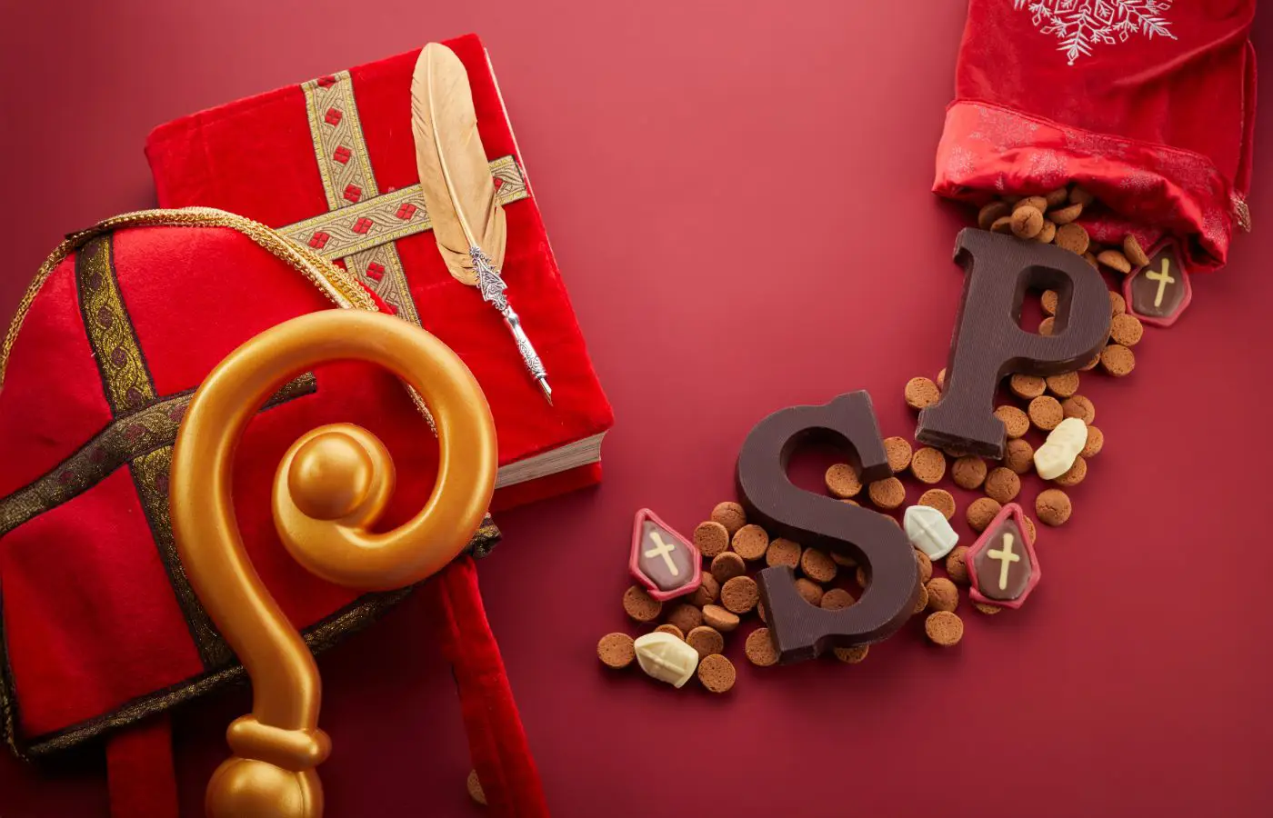 Sinterklaasdecoratie met een staf, rood boek, chocoladeletters S en P, pepernoten, en snoepgoed in een rode zak, symbool van het feest.
