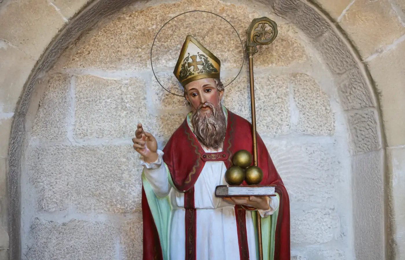 Beeld van Sint-Nicolaas, gekleed in bisschoppelijke gewaden, met mijter, staf en drie gouden ballen, symbool van vrijgevigheid en legendarische verhalen.