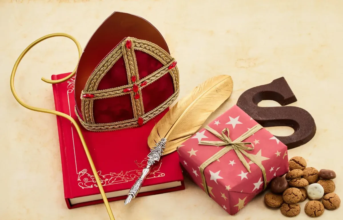 Sinterklaasdecoratie met een mijter, staf, gouden veer, chocoladeletter S, een cadeau met sterrendessin, pepernoten en een rood boek.