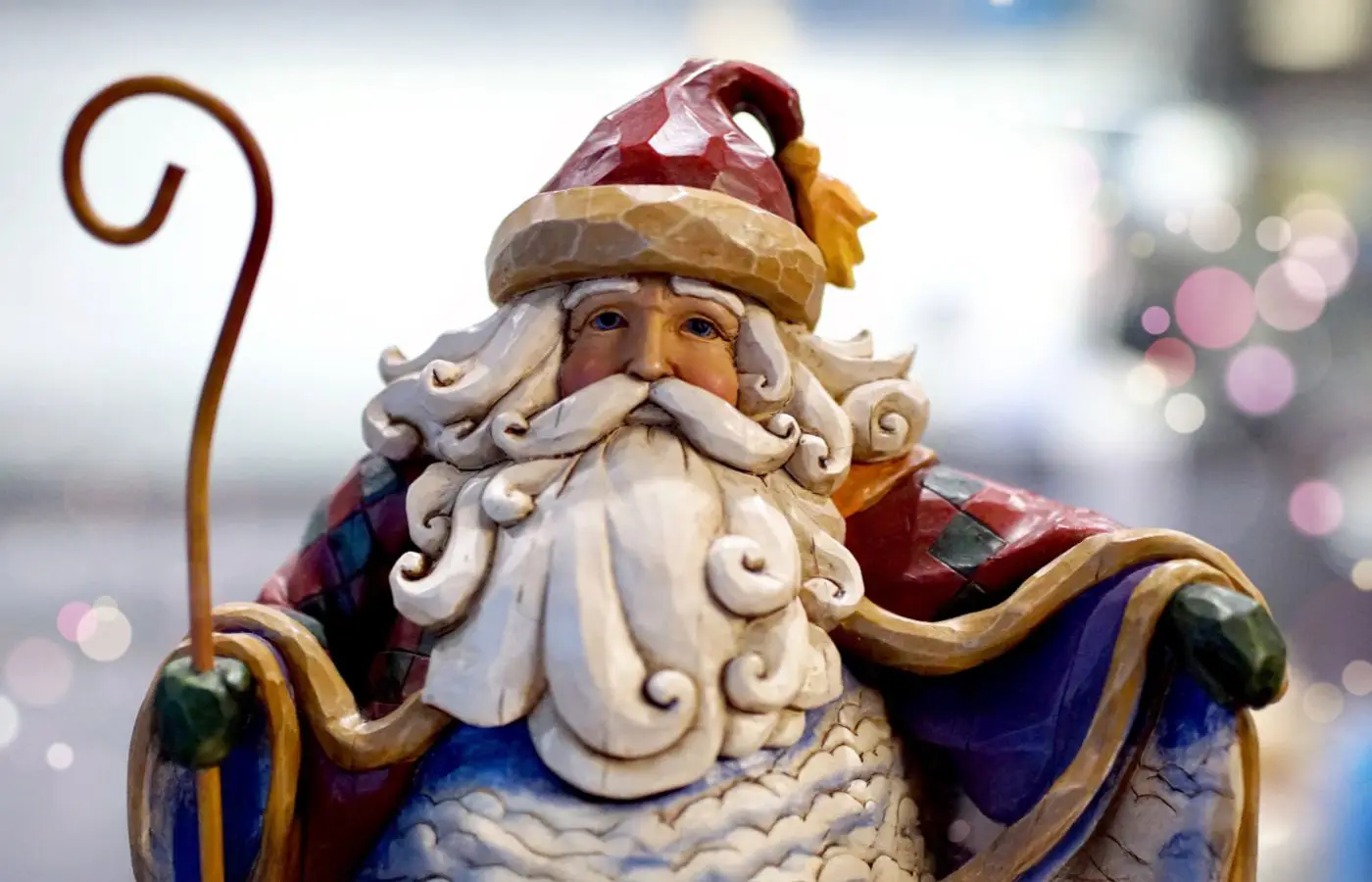 Beeld van Sinterklaas met traditionele rode mijter, witte baard en staf, versierd in een feestelijke sfeer met bokeh-achtergrond.